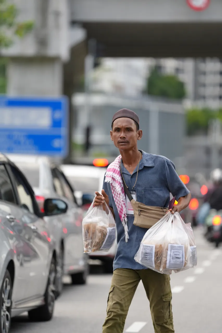 Man in songkok and keffiyeh carrying bags of iftar food — candid Ramadhan portrait