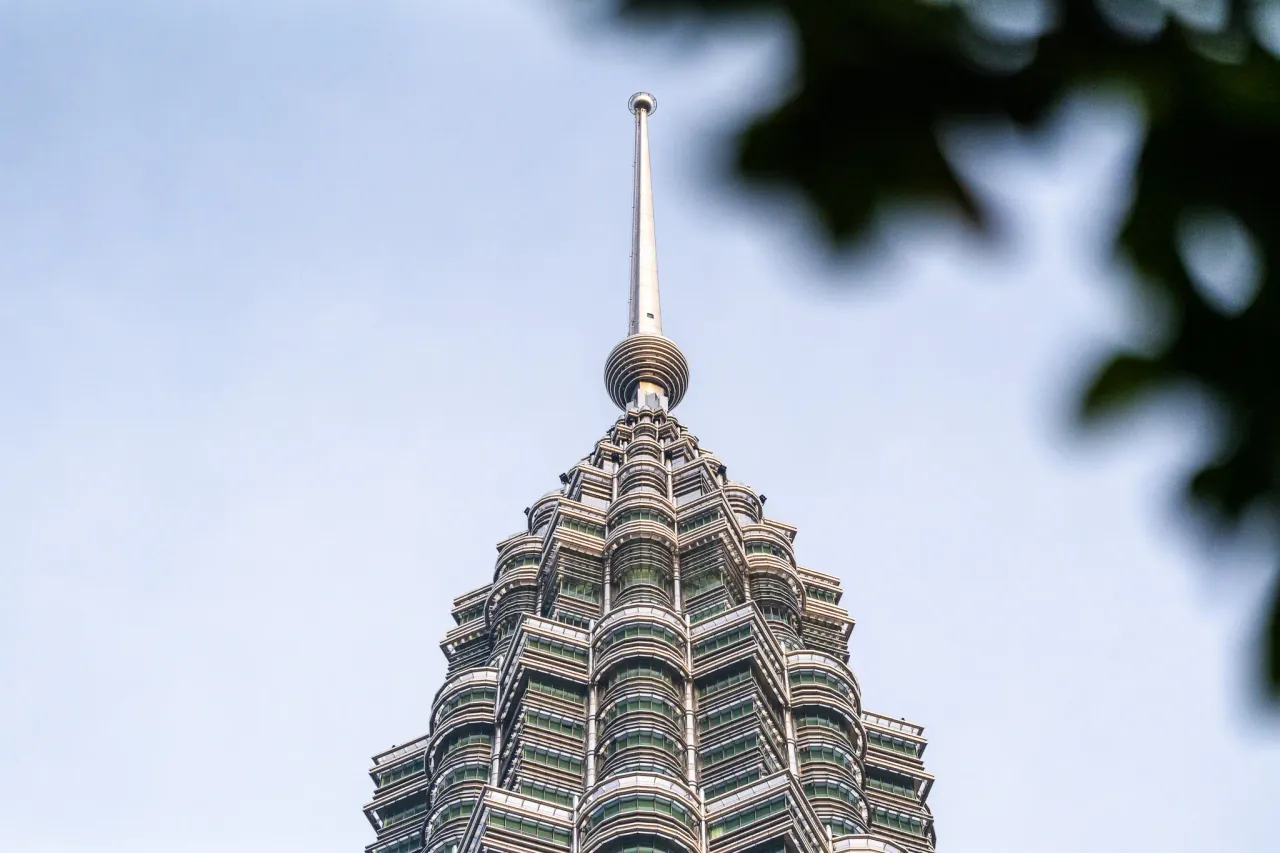 Petronas Tower spire photographed through sunlit leaves — Kuala Lumpur